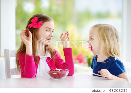 Two pretty little girls eating raspberries at home 43208235