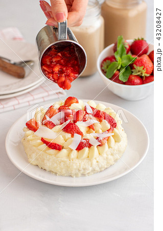 women's hands pour the sauce on the cake. Delicate strawberry cheesecake with coconut. Delicious women's hands pour the sauce on the cake. Delicate strawberry cheesecake with coconut. Delicious 43208427