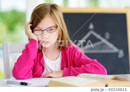 Stressed and tired schoolgirl studying with a pile of books on her desk 43210013