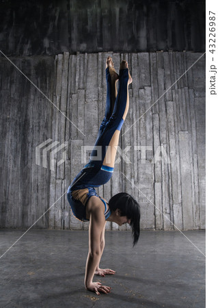Young very flexible female acrobat standing on hand over gray background in photo studio 43226987