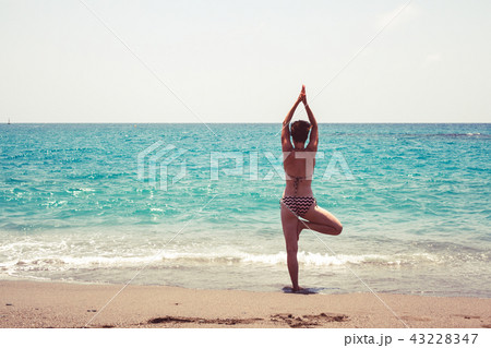 Woman practicing yoga on the shore of the sea 43228347