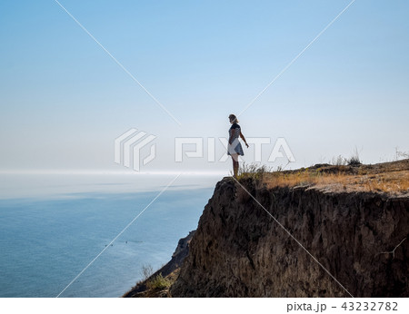 The girl is standing on a cliff near the sea The girl is standing on a cliff near the sea 43232782