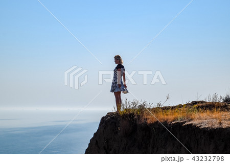 The girl is standing on a cliff near the sea The girl is standing on a cliff near the sea 43232798