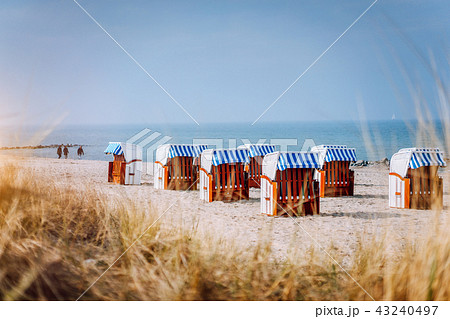 Blue striped roofed chairs on sandy beach on sunny day framed by dune grass in Travemunde. Germany Blue striped roofed chairs on sandy beach on sunny day framed by dune grass in Travemunde. Germany 43240497