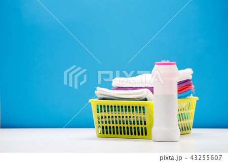Photo of one bottle of cleaning powder and multi-colored towels in basket isolated on blue Photo of one bottle of cleaning powder and multi-colored towels in basket isolated on blue 43255607