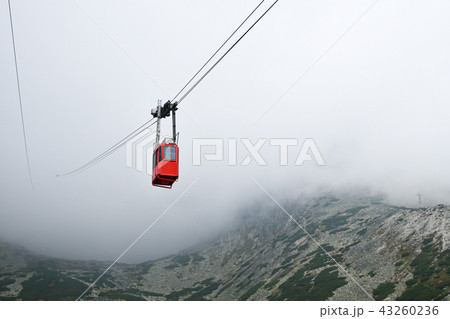 Red mountain cableway car in clouds and fog Red mountain cableway car in clouds and fog 43260236