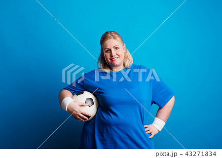 Portrait of a happy overweight woman with a ball in studio on a blue background. 43271834