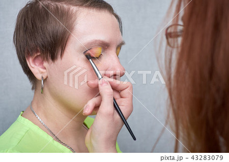 Professional visage artist applying color makeup on woman's face on grey background. Professional visage artist applying color makeup on woman's face on grey background. 43283079