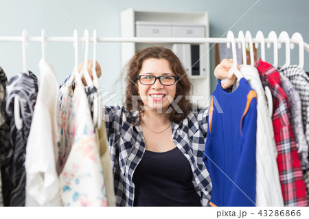 Beauty, fashion and people concept - Beautiful smiling woman in black glasses chooses dresses 43286866