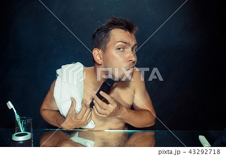 young man in bedroom sitting in front of the mirror scratching his beard 43292718