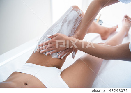 Beautician hands applying cosmetic white clay on lady leg 43298075