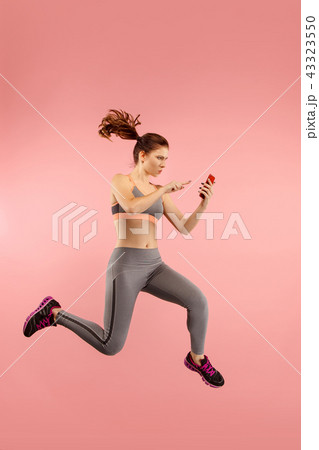 Full length of pretty young woman with mobile phone while jumping 43323550
