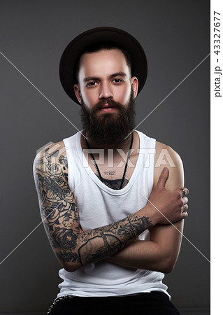Bearded man long beard Brutal tattooed caucasian hipster with moustache  holding cup or mug in rock black style sitting on acid orange chair on  white wooden vintage studio background Stock Photo 