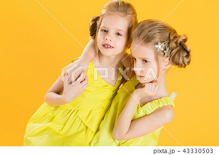 Twins girls are sitting on a chair on a yellow background. Twins girls are sitting on a chair on a yellow background. 43330503