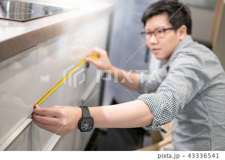 Asian man using tape measure on kitchen counter 43336541