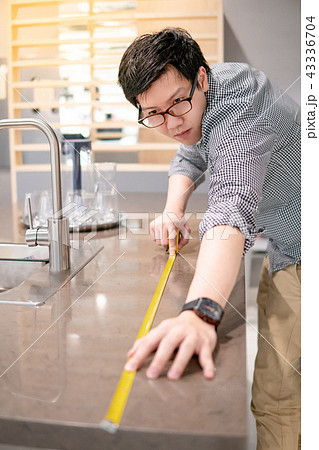 Asian man using tape measure on kitchen counter 43336704