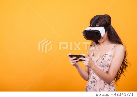 Woman wearing a futuristic looking virtual reality headset goggles in studio over yellow background Woman wearing a futuristic looking virtual reality headset goggles in studio over yellow background 43341771