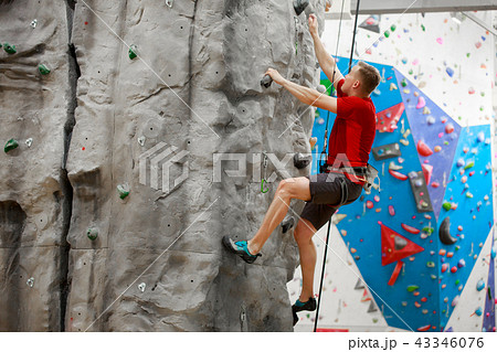 Photo from side of sports man in red T-shirt training on climbing wall 43346076