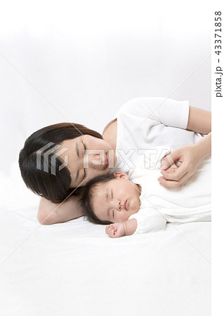 新生児と添い寝しながら赤ちゃんの手を握る若いお母さん 親子の愛と幸せ 母性イメージ コピースペースの写真素材