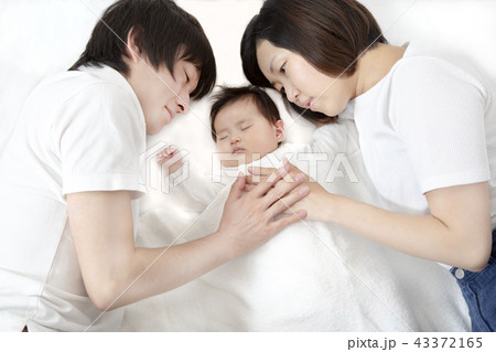 新生児と添い寝し見つめる若い父と母の両親夫婦 幸せな愛ある家族イメージの写真素材