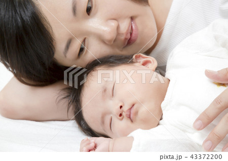 新生児と添い寝しながら赤ちゃんの旨に手を添える若いお母さん 親子の愛と幸せ 母性イメージの写真素材