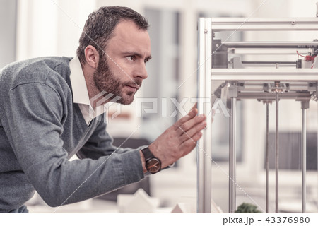 Bearded concentrated adult man watching at 3D printer 43376980