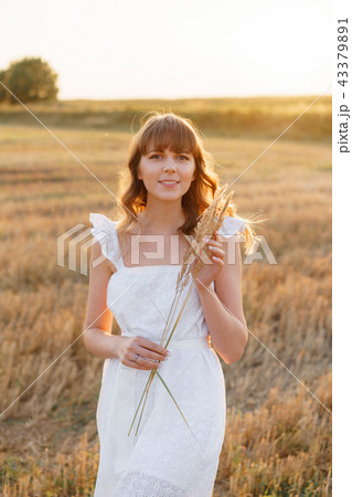 Girl in white dress with spikelets. Woman in field, place for text. Spike and girl in field. Late 43379891