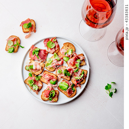 Mini open sandwiches with jamon serrano on white plate and rose wine 43383631