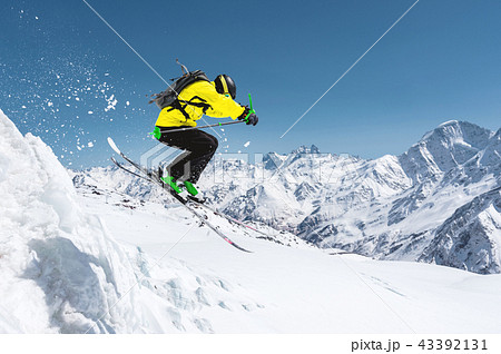 A skier in full sports equipment jumps into the precipice from the top of the glacier against the 43392131
