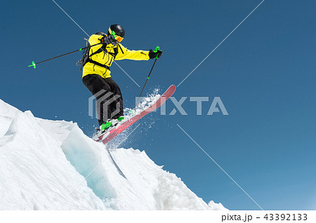 A skier in full sports equipment jumps into the precipice from the top of the glacier against the 43392133