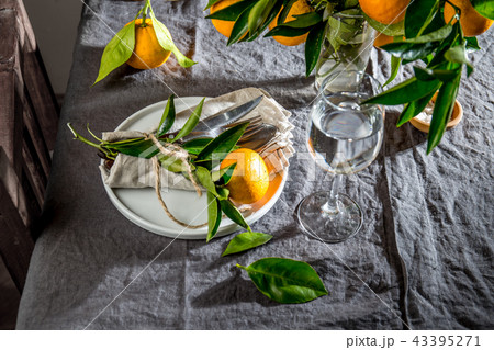 Table setting with white plate, cutlery, linen napkin and orange tree branch decoration on gray 43395271