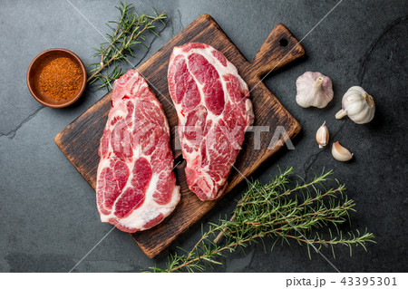 Raw pork steaks with seasoning on wooden board. Gray slate background Raw pork steaks with seasoning on wooden board. Gray slate background 43395301
