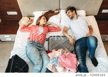 Couple lies on bed with opened suitcase, top view Couple lies on bed with opened suitcase, top view 43400164