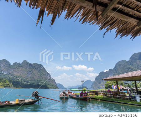 Wooden Thai traditional long-tail boat on a lake with mountains and rain forest in the background Wooden Thai traditional long-tail boat on a lake with mountains and rain forest in the background 43415156
