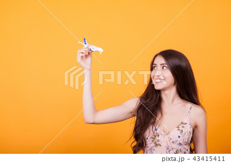 Young beautiful woman playing with toy plane in studio over yellow background Young beautiful woman playing with toy plane in studio over yellow background 43415411