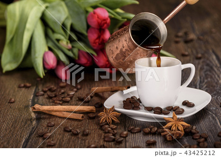 Pouring coffee into a white cup against the background of tulips close up 43425212