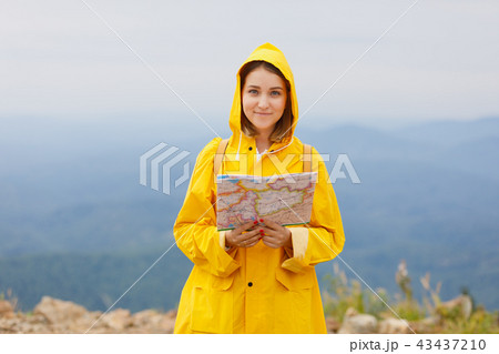 Hipster young girl in yellow raincoat with backpack on peak of mountain, looking map. Tourist 43437210