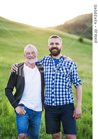 A portrait of an adult hipster son with senior father in nature at sunset. A portrait of an adult hipster son with senior father in nature at sunset. 43439040