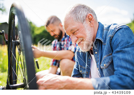 An adult hipster son and senior father repairing bicycle outside on a sunny day. 43439109