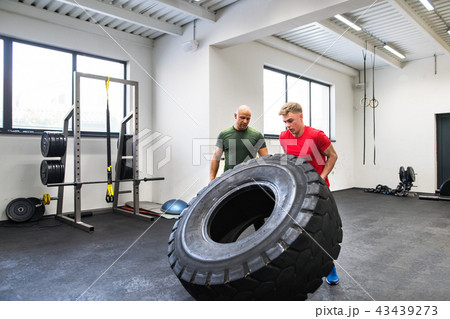 Fit young man with a personal trainer in gym working out, moving tire. Fit young man with a personal trainer in gym working out, moving tire. 43439273