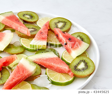 Pattern of pieces of watermelon, kiwi, lime and melting ice cubes in a plate on a gray marble 43445625