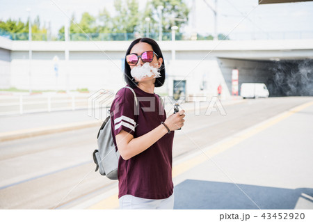 Vaping. Young beautiful woman smoking e-cigarette with smoke outdoors. Vapor concept. 43452920