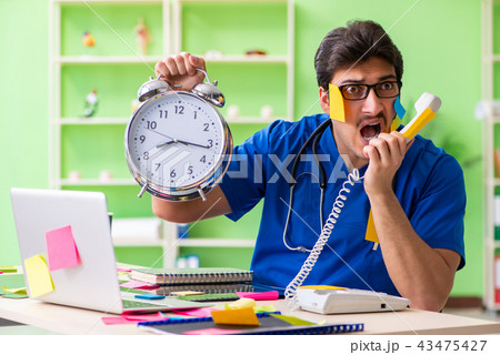 Young doctor sitting in hospital with many conflicting prioritie Young doctor sitting in hospital with many conflicting prioritie 43475427