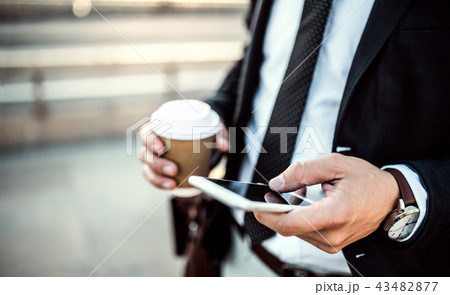 A close-up of a businessman with smartphone and coffee in the city, texting. A close-up of a businessman with smartphone and coffee in the city, texting. 43482877
