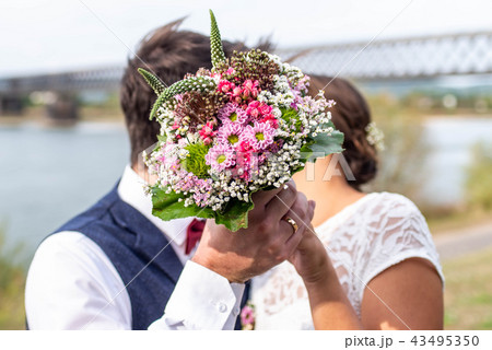 Side view of loving wedding couple kissing behind bouquet in garden Side view of loving wedding couple kissing behind bouquet in garden 43495350