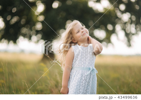 Little girl in sky blue dress stand in field in front of big tree Little girl in sky blue dress stand in field in front of big tree 43499636