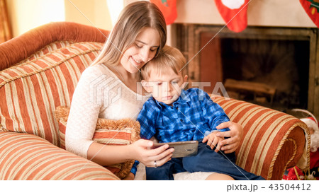 Portrait of beautiful smiling young woman resting in armchair with her little boy and watching Portrait of beautiful smiling young woman resting in armchair with her little boy and watching 43504412