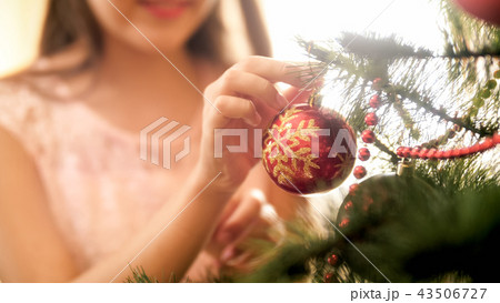 CLoseup image of young woman putting red decorative babubles on Christmas tree branch CLoseup image of young woman putting red decorative babubles on Christmas tree branch 43506727