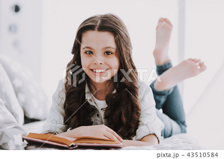 Cute Little Girl Lying on Bed and Reading Book 43510584