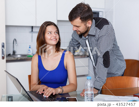 Young woman looking at laptop and man standing at home Young woman looking at laptop and man standing at home 43527457